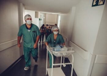 Healthcare workers in surgical attire transporting a newborn in a hospital corridor.