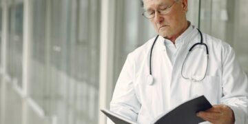 Elderly doctor with stethoscope attentively reading a medical report in a modern hospital setting.