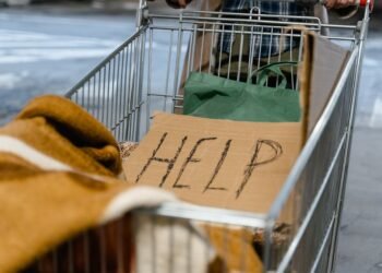 A shopping cart with a cardboard 'Help' sign and belongings, symbolizing urban homelessness.