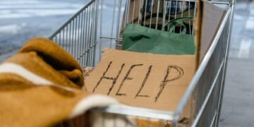 A shopping cart with a cardboard 'Help' sign and belongings, symbolizing urban homelessness.